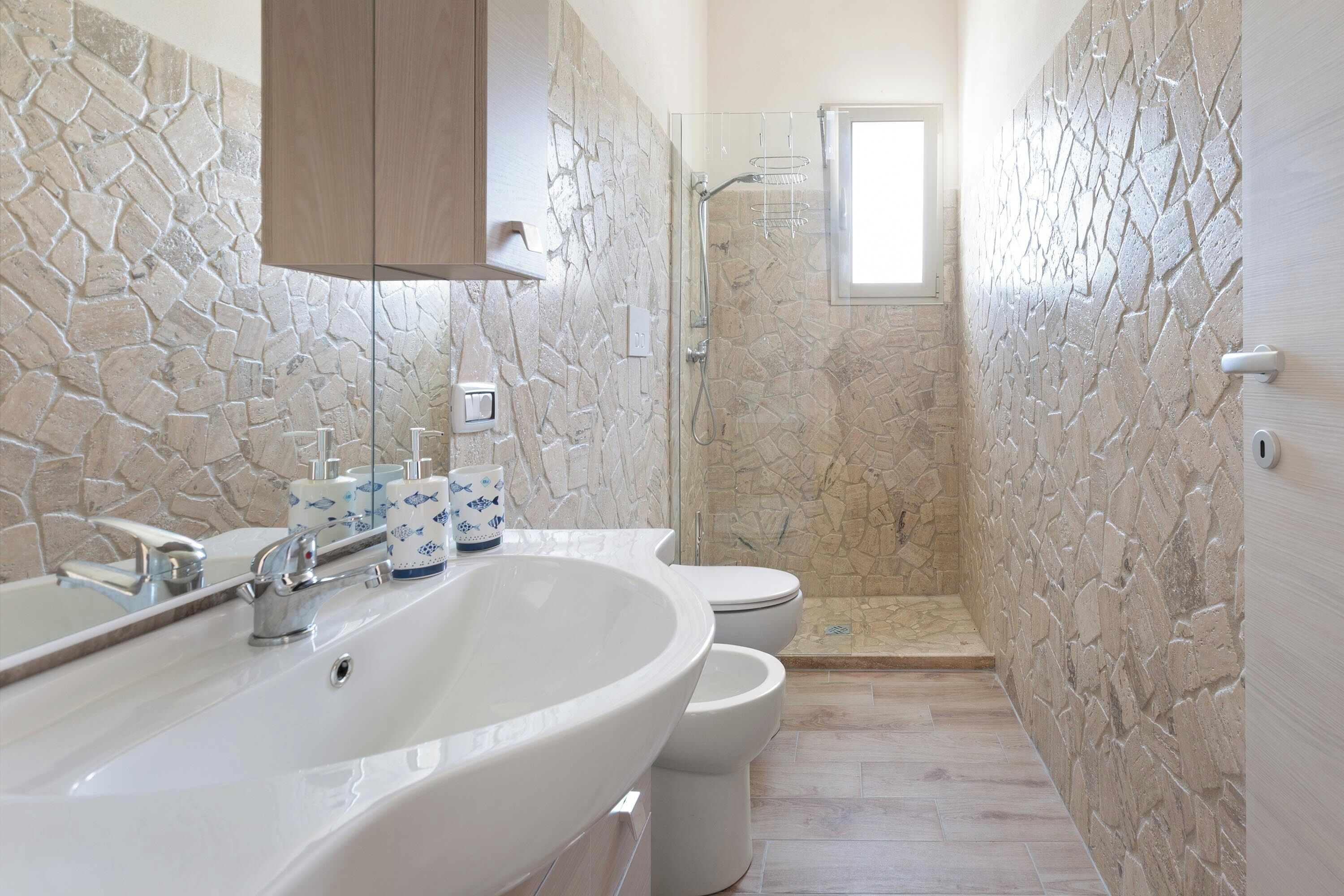 Un bagno con parete in pietra, un lavandino grande, un water e un box doccia.