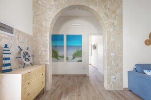 Ein Zimmer mit einem Steingewölbe, Holzboden, einem blauen Sofa, einer Holzkommode und zwei Bildern einer Strandansicht.