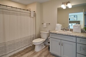 Un baño con cortina de ducha, inodoro, lavamanos y armarios.