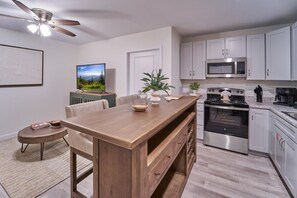 A modern kitchen with white cabinets, stainless steel appliances, a wooden island, and a ceiling fan. - The Ruby 104 (Pigeon Forge)