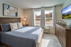 Un dormitorio con cama, mesitas de noche, cómoda, televisor y ventana con cortinas.
