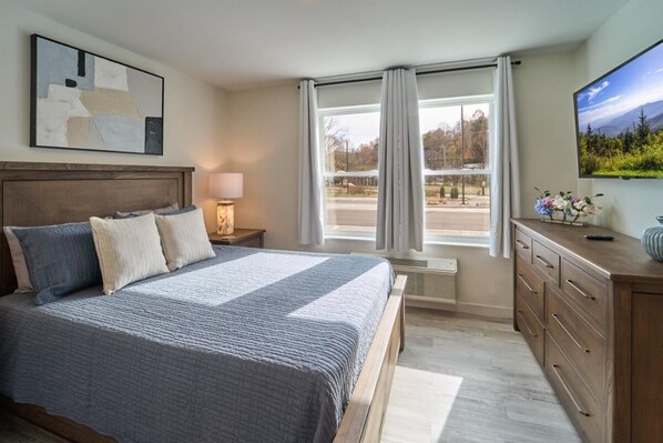 A bedroom with a bed, nightstands, a dresser, a TV, and a window with curtains. - The Ruby 104 (Pigeon Forge)