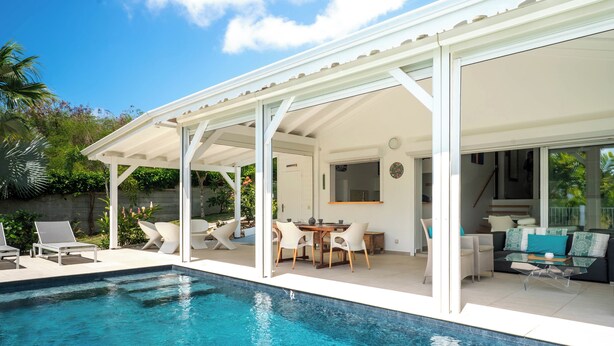 Ein Poolbereich mit überdachter Terrasse, Liegestühlen, Esstisch und einer Couch.