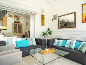 Ein modernes Wohnzimmer mit einem Glastisch, dunklen Sofas mit gemusterten Kissen, einem Holzschrank und einem großen Spiegel.