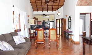 Una sala de estar con sofá, sillas de madera, una mesa de comedor y una cocina al fondo.