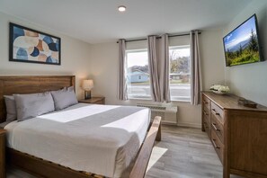 Ein Schlafzimmer mit einem Bett, einem Nachttisch, einem Fernseher, einem Fenster mit Vorhängen und einem Bild an der Wand.