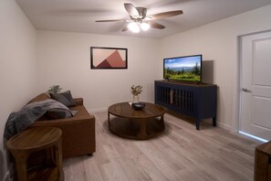 A living room with a sofa, a round coffee table, a television on a cabinet, a ceiling fan, and a door. - The Ruby 108 (Pigeon Forge)