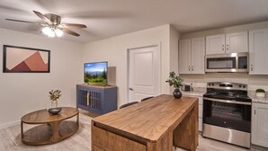 Une cuisine moderne dotée d’un îlot central en bois, d’appareils électroménagers en acier inoxydable et d’un ventilateur de plafond.