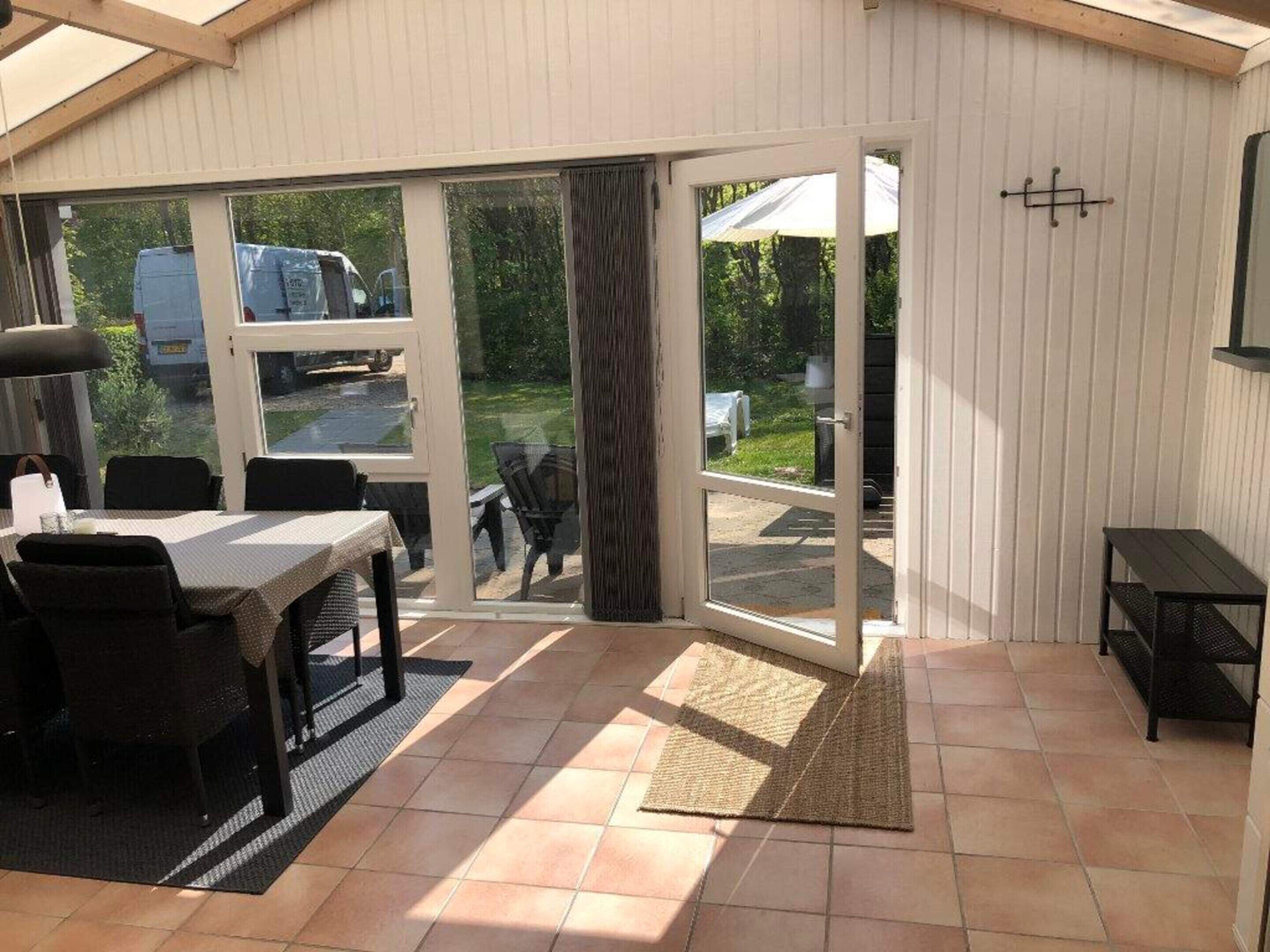 Une terrasse ensoleillée avec une table et des chaises, une porte-fenêtre coulissante et une petite table noire.