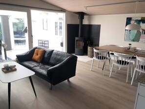 A modern living room with a black leather sofa, a white table, and a dining area with white chairs. - 4 Star Holiday Home in Esbjerg V (Esbjerg)