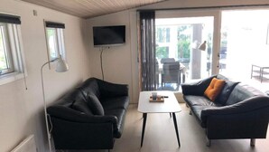 A living room with two black leather sofas, a white coffee table, a floor lamp, and a TV mounted on the wall. - 4 Star Holiday Home in Esbjerg V (Esbjerg)