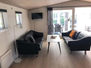 A living room with two black leather sofas, a white coffee table, a floor lamp, and a TV mounted on the wall. - 4 Star Holiday Home in Esbjerg V (Esbjerg)