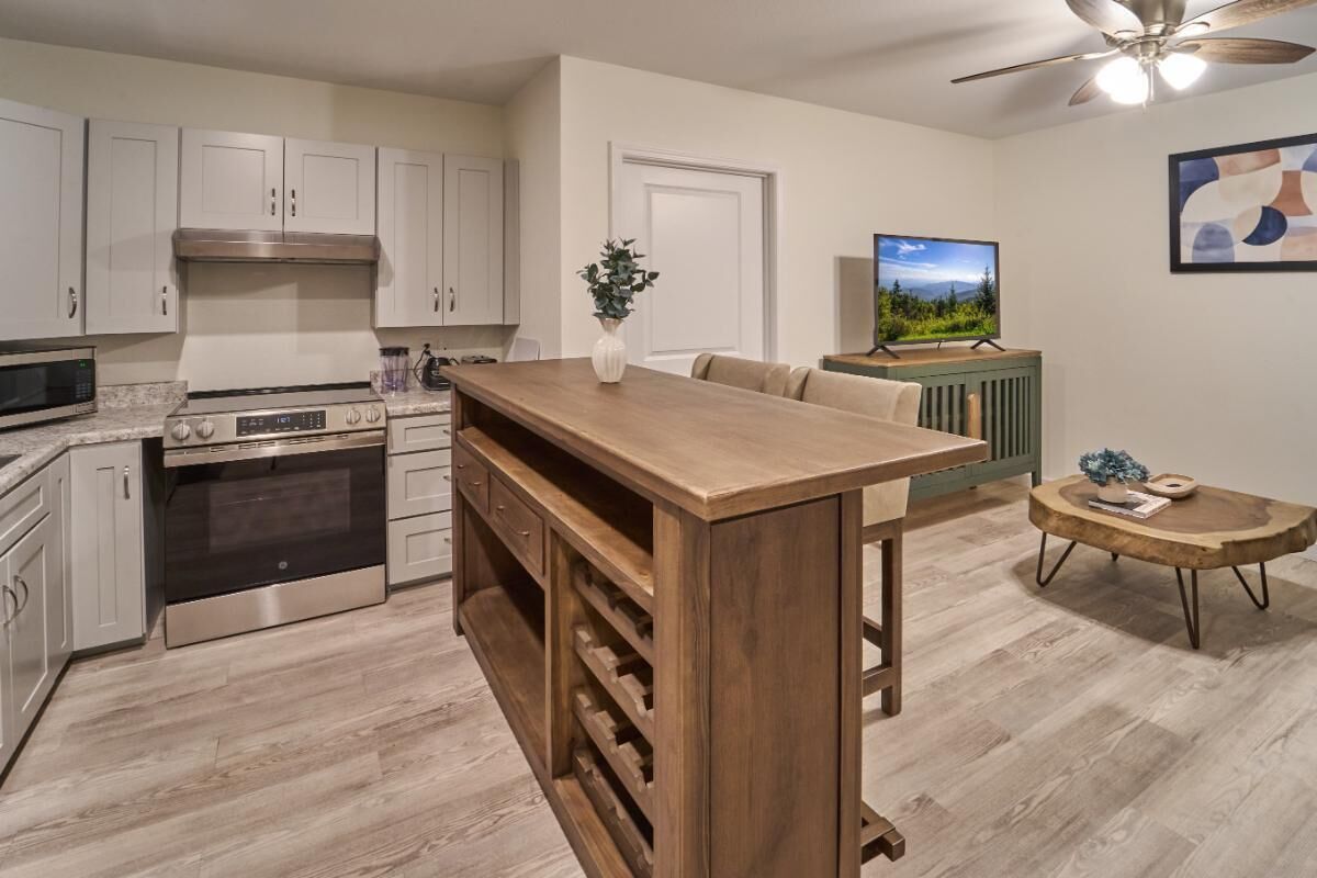 A modern kitchen with white cabinets, a wooden island, stainless steel appliances, and a dining area with a sofa and coffee table.