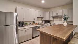 Una cocina moderna con electrodomésticos de acero inoxidable, armarios de tonos claros, una isla de madera y un taburete de bar.