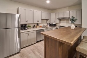 A modern kitchen with stainless steel appliances, light-colored cabinets, a wooden island, and a bar stool. - The Ruby 109 (Pigeon Forge)