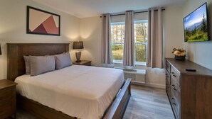 A bedroom with a large bed, a nightstand, a dresser, a lamp, a window with curtains, and a painting on the wall. - The Ruby 111 (Pigeon Forge)