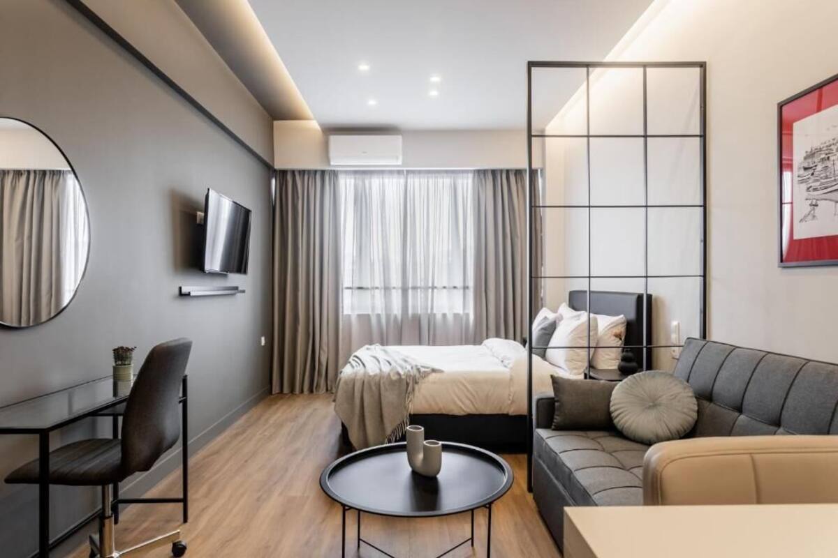 A modern hotel room with a bed, a sofa, a TV, and a round table.