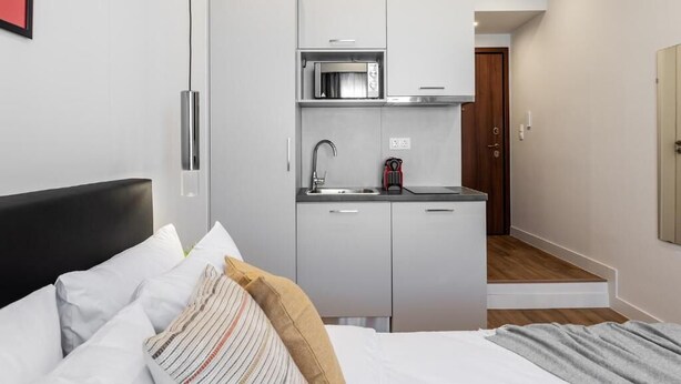 Ett kompakt hotellrum med en säng, ett litet kök och ett trägolv.