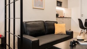 Ett modernt vardagsrum med en svart lädersoffa, ett soffbord och ett kök i bakgrunden.