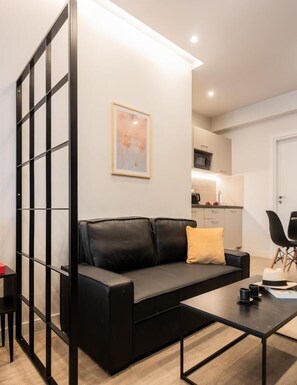 Ein modernes Wohnzimmer mit einer schwarzen Ledersofa, einem Couchtisch und einer Küche im Hintergrund.