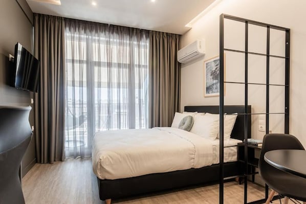 A modern hotel room with a bed, a desk, a chair, a TV, and a window with curtains. - Au Piree by Calon (Pireas)