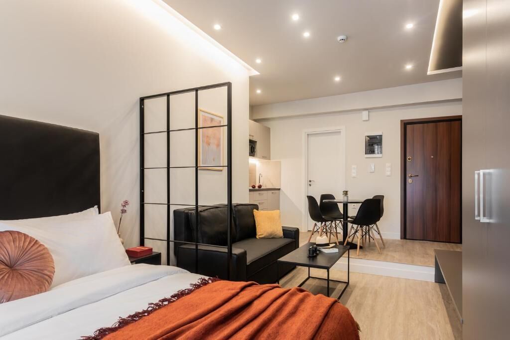 Ein modernes Hotelzimmer mit Bett, einer Couch, einem Esstisch mit Stühlen, einer Küchenzeile und einer separaten Tür.