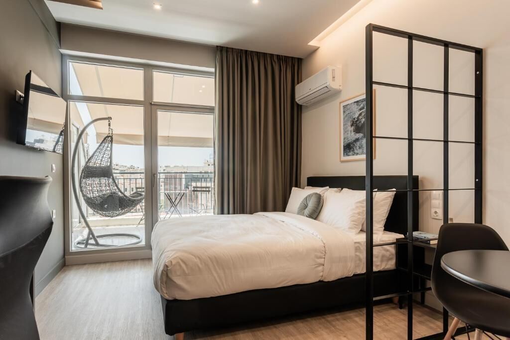 Ein modernes Hotelzimmer mit Bett, Sessel, Schreibtisch, großem Fenster und Blick auf die Stadt.