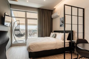 Ein modernes Hotelzimmer mit Bett, Sessel, Schreibtisch, großem Fenster und Blick auf die Stadt.