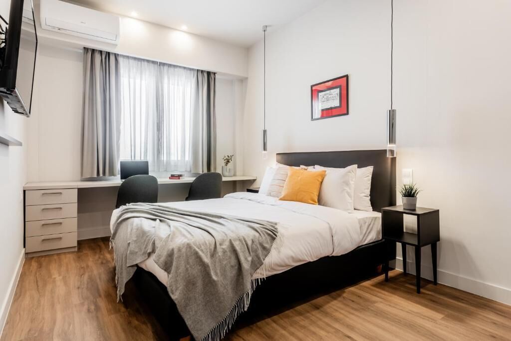 Ein Schlafzimmer mit Bett, Nachttisch, Schreibtisch, Stuhl und Klimaanlage.