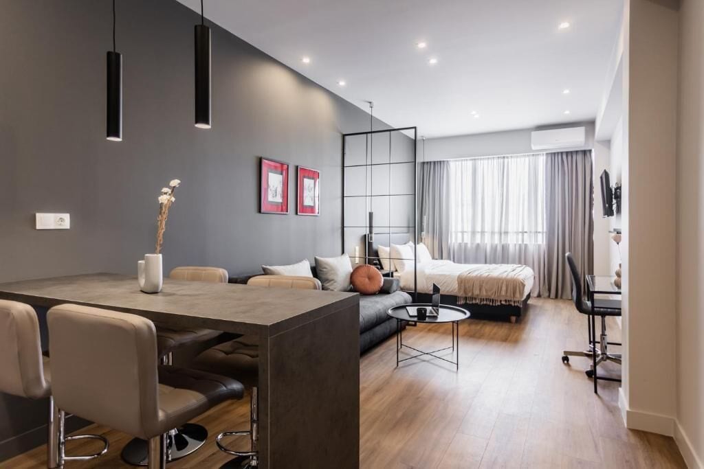 Una habitación de hotel moderna con zona de comedor, sofá, cama y escritorio.