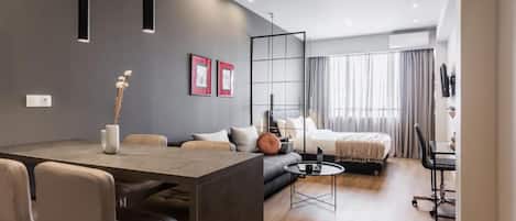 Una habitación de hotel moderna con zona de comedor, sofá, cama y escritorio.