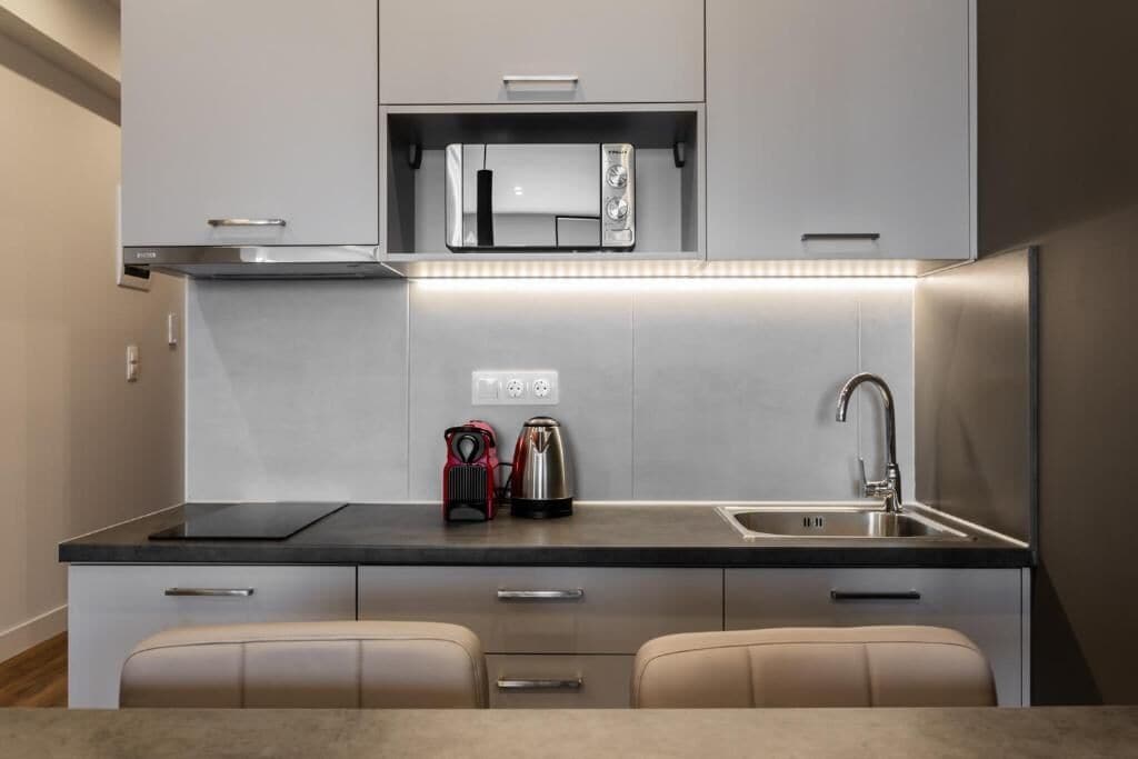 A compact kitchen with a microwave, kettle, and sink.