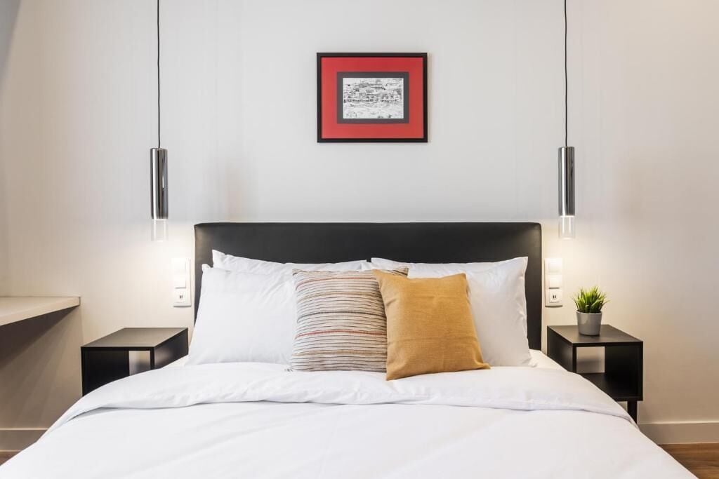 A neatly made bed with white bedding, a black headboard, and two bedside tables with a small potted plant on one.