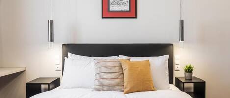 A neatly made bed with white bedding, a black headboard, and two bedside tables with a small potted plant on one.