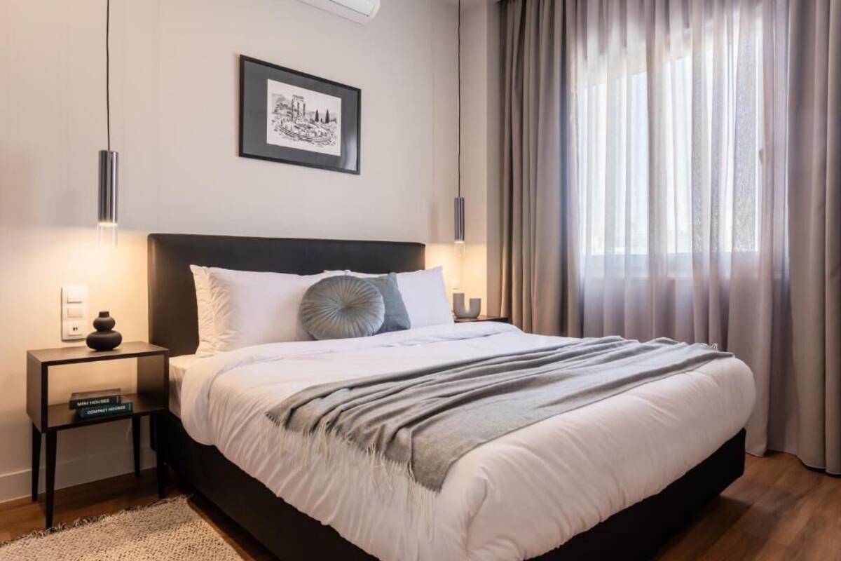 A modern bedroom with a large bed, bedside tables, a framed picture, and sheer curtains.