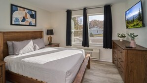 Um quarto com uma cama de madeira, uma mesinha de cabeceira, um penteado, uma janela com cortinas e um quadro na parede.