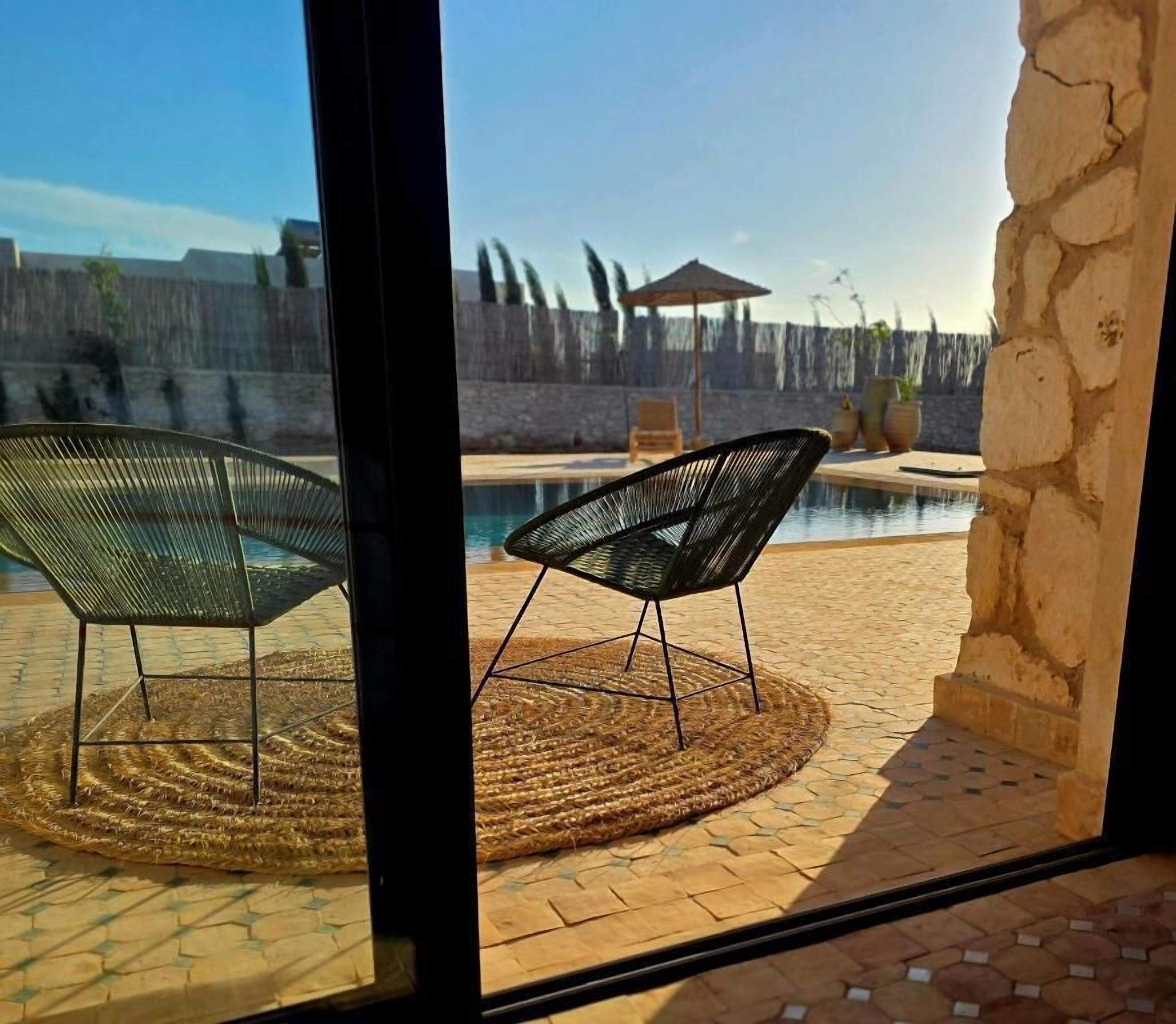 Une piscine avec deux chaises, un tapis en fibres naturelles et un mur en pierre.
