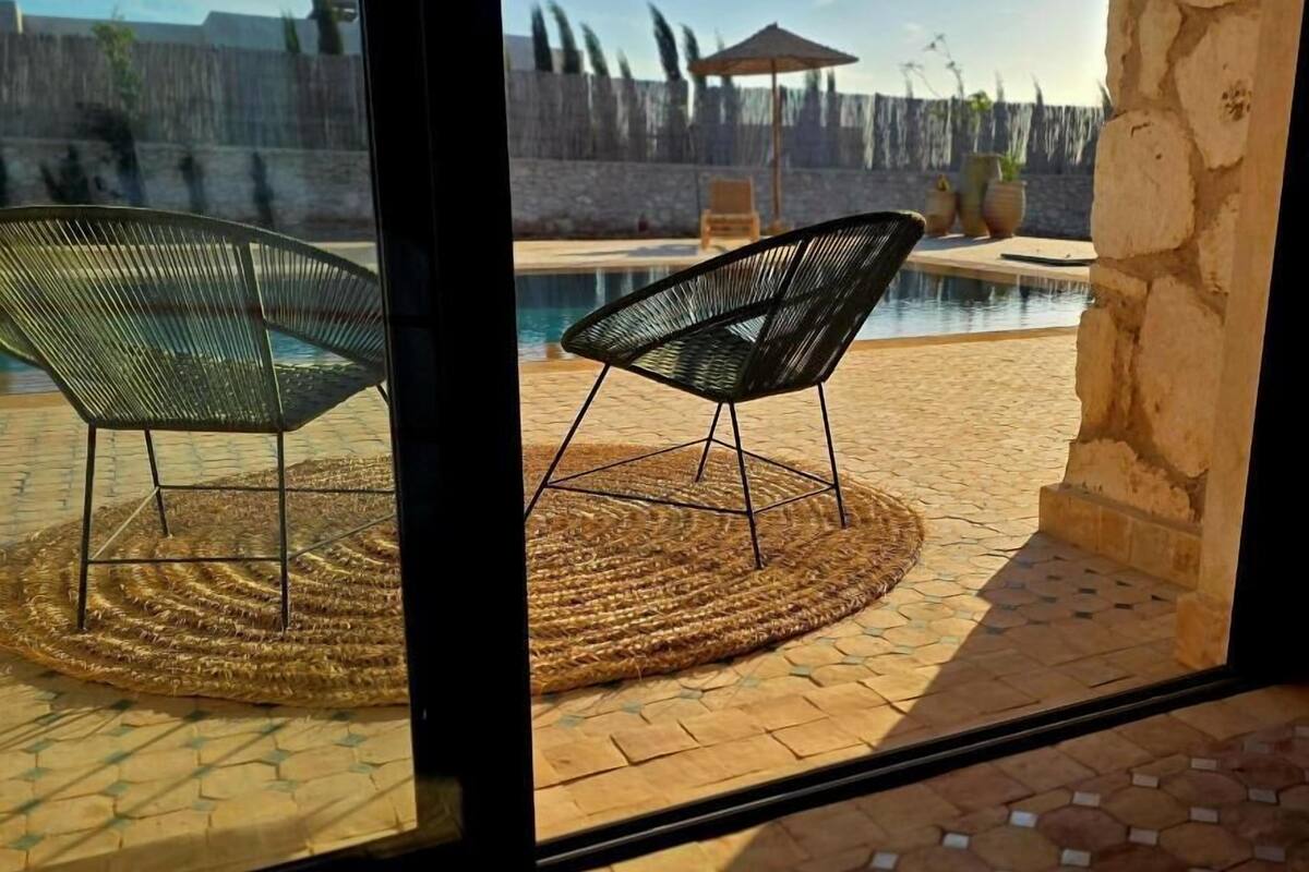 A view of a swimming pool with two chairs, a woven mat, and a stone wall.