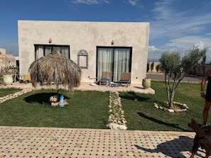 A modern building with a thatched roof, a paved patio, and a small garden with a tree and a sheep. - TEMPO Vegan B&B (Essaouira)