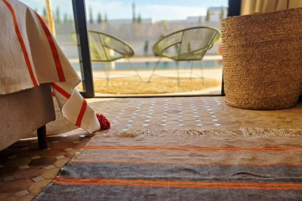 Une chambre avec un lit, un panier en osier et une vue sur un espace extérieur aménagé avec des chaises et une piscine.