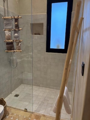 A glass-enclosed shower with a view of the sky, a wooden rack, and a small shelf.