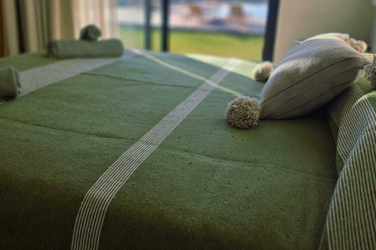 A room with a bed, pillows, and a view through a window.