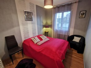 A bedroom with a red bed, a chair, a lamp, and a window with curtains. - Holiday Home 'Gîte À Proximité De Blois Chambord' with Private Terrace, Private Garden and Wi-Fi (Les Montils)