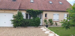 Uma casa com telhado de telhas vermelhas, porta de garagem branca e entrada com caminho de cascalho.