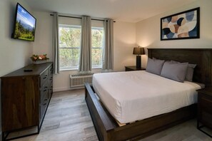 A bedroom with a bed, a dresser, a TV, a window with curtains, a lamp, and a painting. - The Ruby 113 (Pigeon Forge)