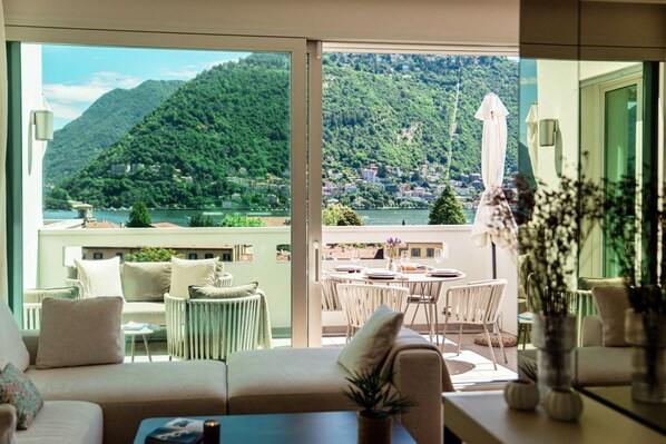 A room with a balcony overlooking a lake and mountains, furnished with a sofa, chairs, and a dining table. - Suite Prestige - by MyHomeInComo (Como)