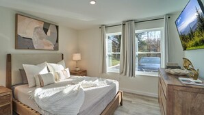 A bedroom with a bed, bedside tables, a lamp, a dresser, a painting, and a window with curtains. - The Ruby 114 (Pigeon Forge)