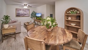 A dining area with a round wooden table, chairs, a ceiling fan, a television, and a bookshelf with flowers. - The Ruby 114 (Pigeon Forge)