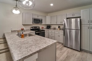 A modern kitchen with white cabinets, stainless steel appliances, granite countertops, and pendant lighting. - The Ruby 115 (Pigeon Forge)