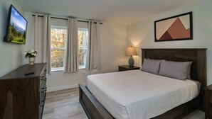 A bedroom with a bed, a nightstand, a lamp, a dresser, a TV, and a window with curtains. - The Ruby 115 (Pigeon Forge)